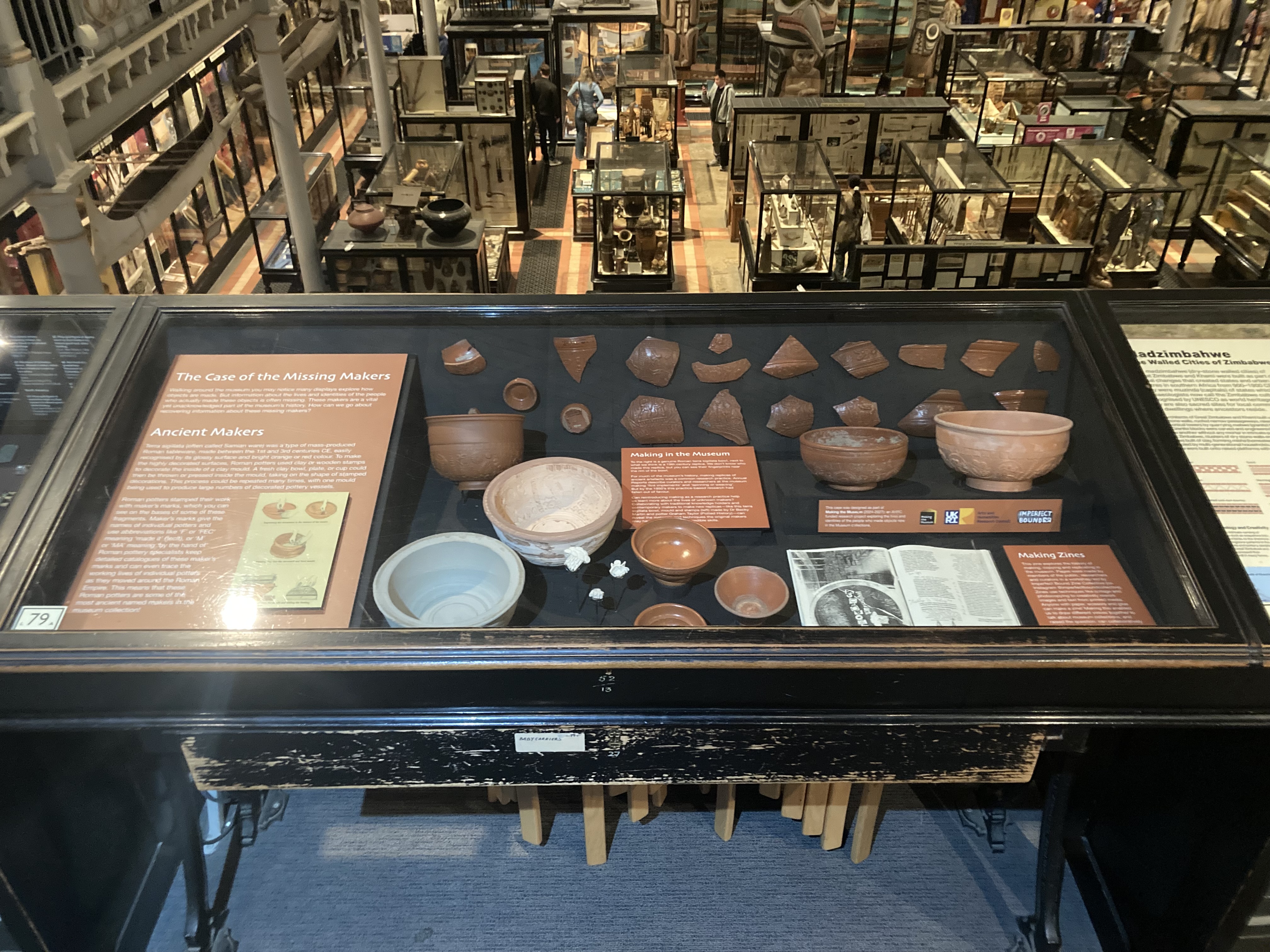 Waist-height museum display case filled with pottery, shards, and a magazine