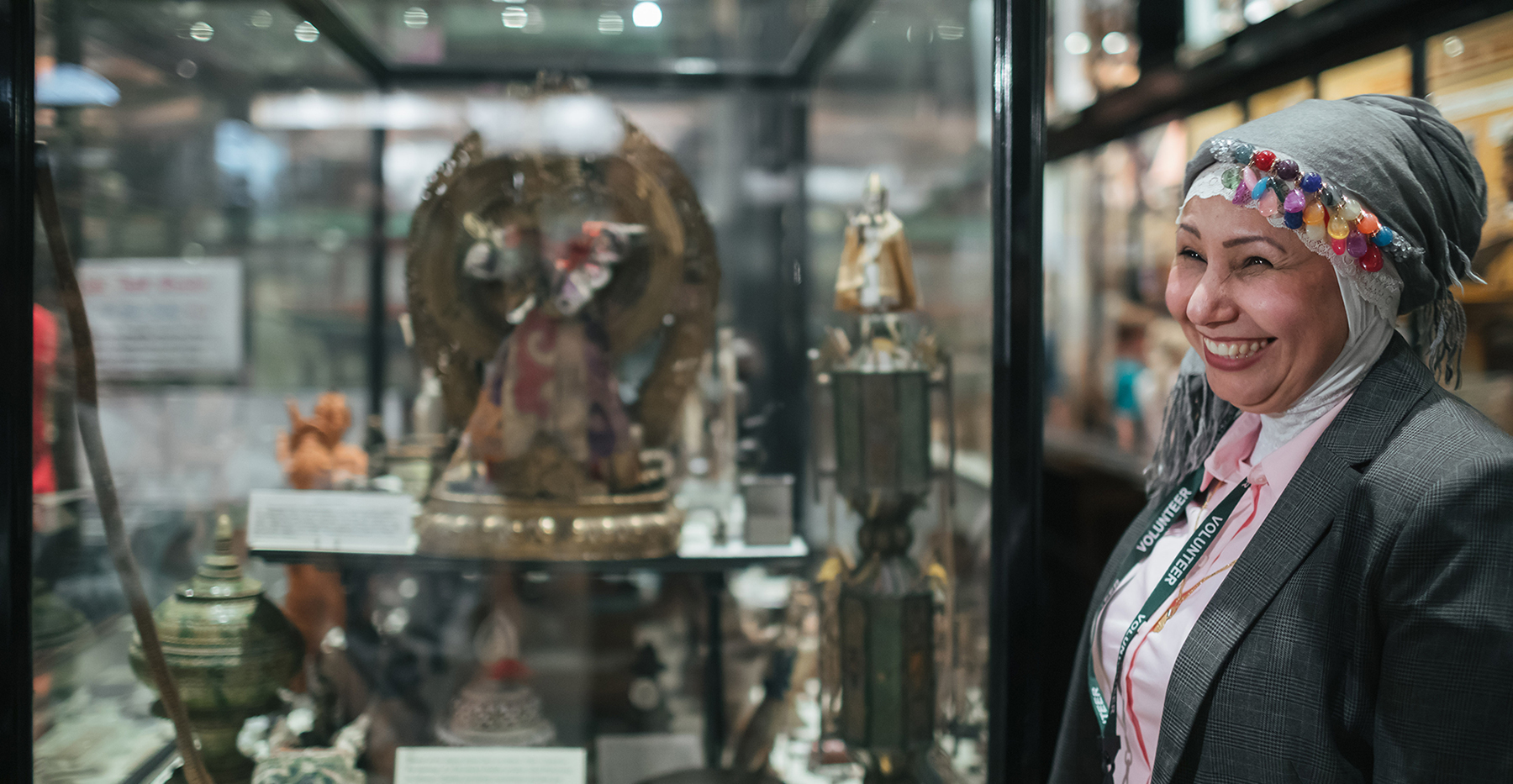 A woman smiles while pointing to an object in a glass display case 