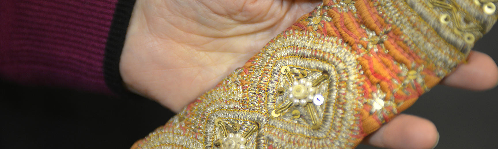 Hand holding a textile richly decorated with metallic threads, beads and sequins