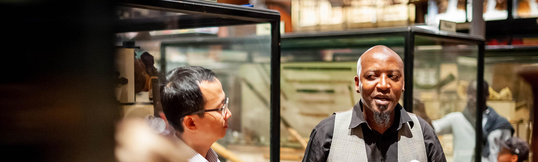 A man talks to a group of people gathered around a museum display case 