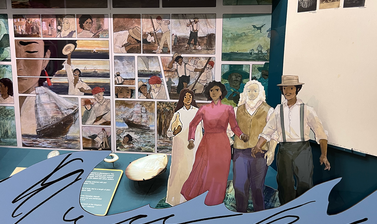 Close up view showing a museum display containing a graphic comic background, cut out illustrated figures, and a wave graphic across the bottom of the case.