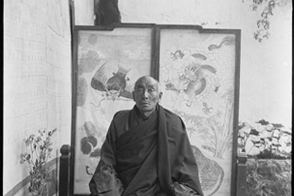 portrait photo of a robed man sitting in front of two patterned panels 