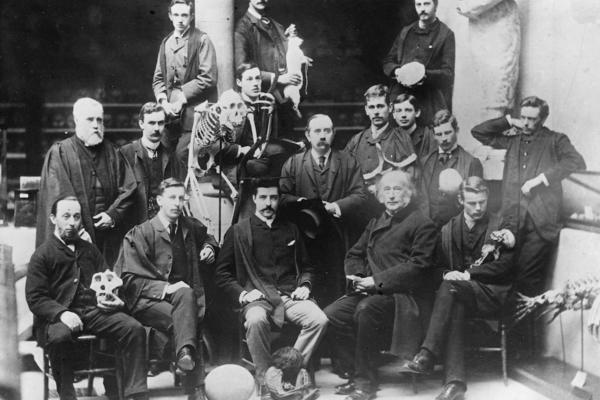 group black and white portrait photo of men posing with a variety of museum objects