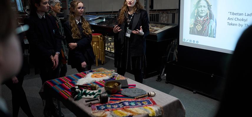 Teaching session in the museum with a screen showing a photograph of a Tibetan woman and a table covered with objects from the collections.