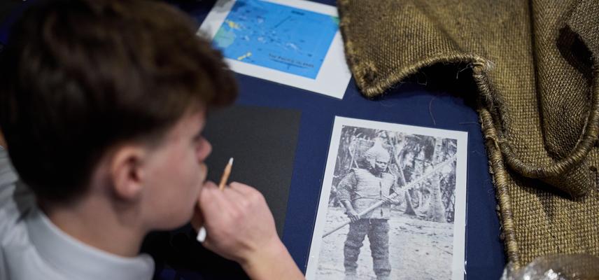 School student looking at a black and white photo next to garment laid on blue table top.