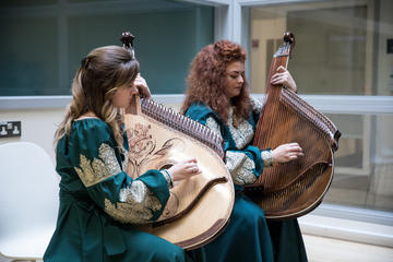 Two women wearing blue embroidered dresses playing traditional stringed Ukrainian instruments.