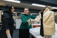 Two woman stand in a research space at a museum admiring a gold brocade scarf displayed on a torso mannequin