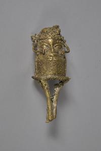 A rough bronze figure of a head with ornaments, with three bronze runners emerging from the base